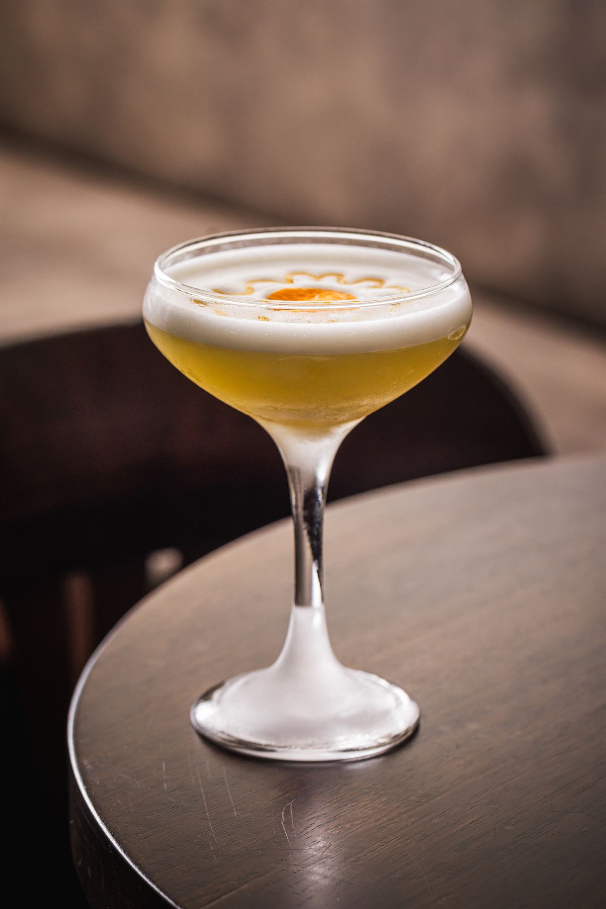 Luna Sour — egg-white cocktail with orange flower art, on a timber table